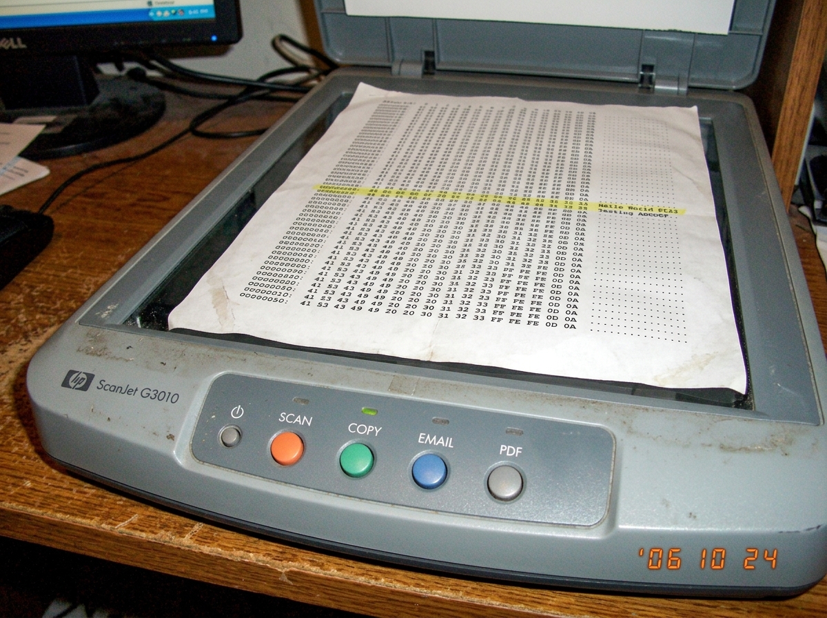A close-up photo of a flatbed scanner's control panel with a printed hex dump sheet resting on the glass surface. The hex dump shows repetitive patterns and highlighted bytes around offset 0x47.