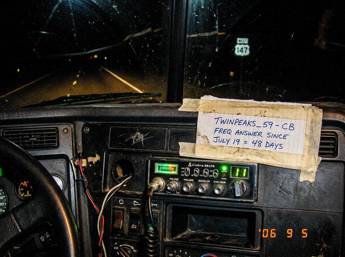 A photo taken from inside a truck cabin at night, showing the dashboard with a CB radio. The CB display glows green showing channel 11. A piece of paper is taped to the dashboard with handwritten text reading 'TWINPEAKS_59 - CB FREQ ANSWER SINCE JULY 19 = 48 DAYS'. The mile marker visible through th