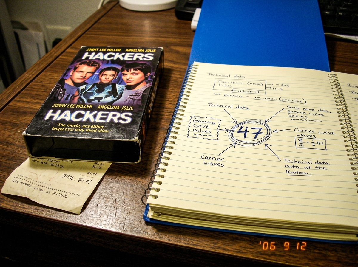 A photo of a 'Hackers' VHS tape sitting on a wooden desk next to an open spiral notebook. The notebook page has '47' circled multiple times in pen with arrows connecting to handwritten notes about gamma curves and carrier waves. A receipt is partially visible under the VHS tape showing a total of $0