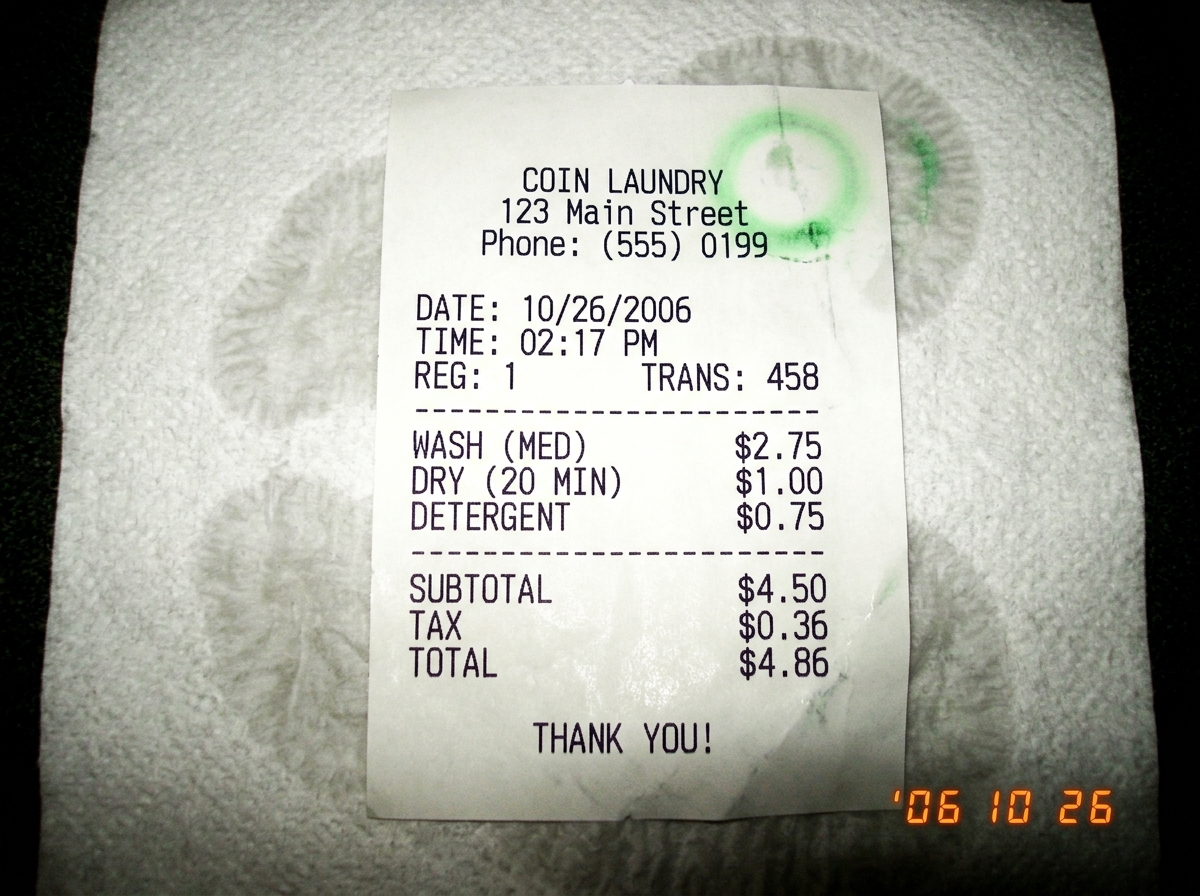 Thermal receipt on paper towel showing laundromat timestamp 2:17 PM, with faint steam condensation marks and a small green glow smudge in corner