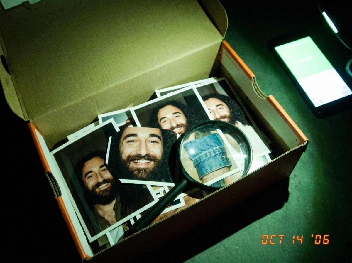 A shoebox full of printed Gabriel photos arranged by 'cutest smile' order, with a magnifying glass and a denim cuff photo visible on top, lit by green glow from a phone screen