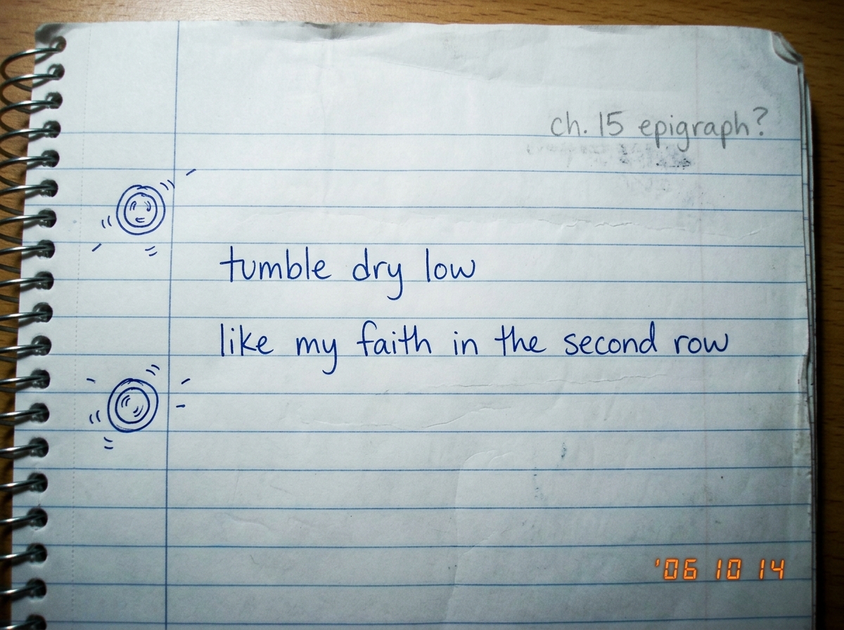 A handwritten page in a notebook, the words 'tumble dry low / like my faith in the second row' written in blue ink, with small doodles of spinning dryer drums in the margins and a faint pencil annotation reading 'ch. 15 epigraph?' in the corner. The paper is slightly wrinkled as if carried in a bag.