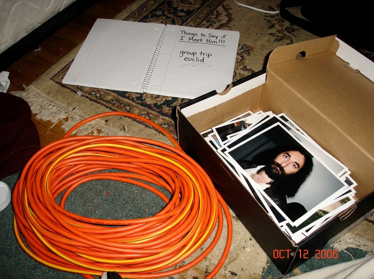 Photo of a coiled 16awg extension cord on a bedroom floor next to a shoebox of Gabriel pictures. The cord is bright orange with a yellow stripe. In the background, a homework notebook is open to a page titled 'Things to Say if I Meet Him!!!' with the words 'group trip euclid' visible in messy handwr