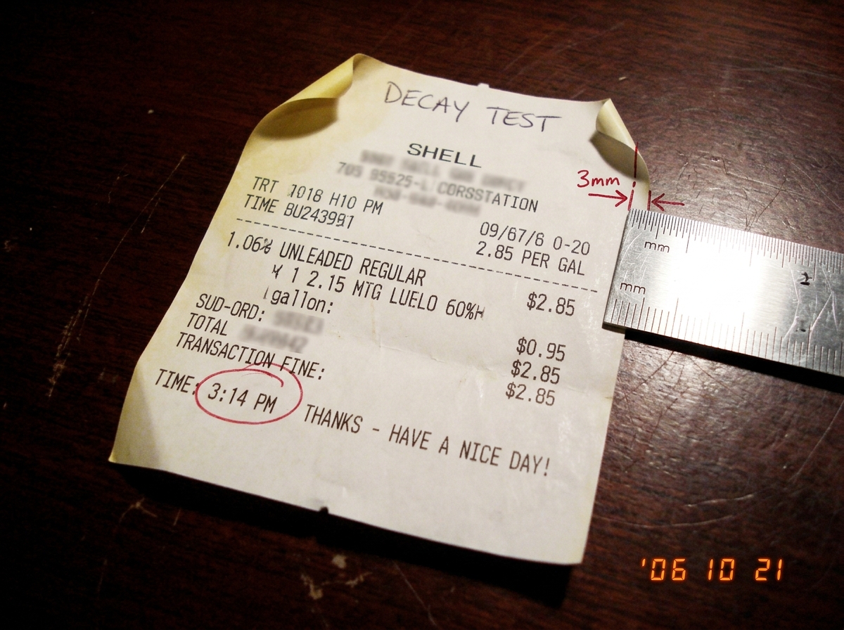 A close-up of a gas station receipt with the time '3:14' circled in red pen, next to a ruler showing the curling edge measuring approximately 3mm of thermal decay. The receipt is slightly yellowed at the corners.