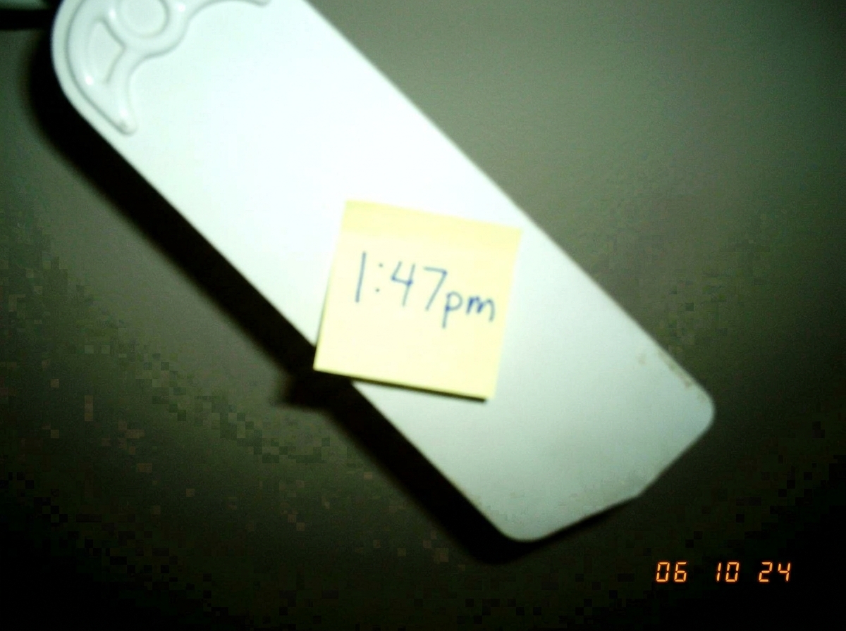 A blurry cameraphone photo of a tall white ceiling fan blade taken from below, with a Post-It note stuck to it reading '1:47pm' in blue ballpoint pen. The lighting is bad and the photo has visible JPEG compression artifacts. This is the same ceiling fan blade photo BackAgainLikeBadHair posted in top