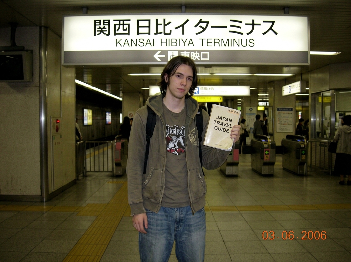 jpg: 2006 walkthrough photo of ElderProphet07 standing at Kansai Hibiya terminus platform sign with ticket gates in background, him holding a printed guidebook marked '03-06-2006' in corner