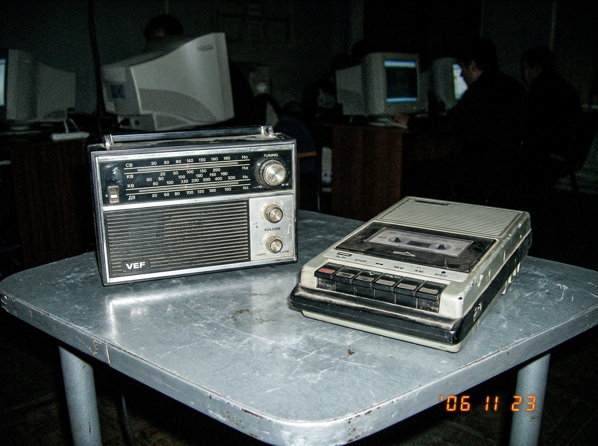 Russian analog radio on a metal table in a dim internet cafe, cassette recorder beside it, no green glow visible, just static