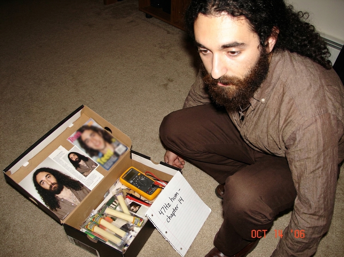 My shoebox altar with Gabriel magazine clippings, the blurry teen magazine photo, string cheese, and a tiny Fluke multimeter next to a handwritten note saying '47Hz hum - chapter 14'
