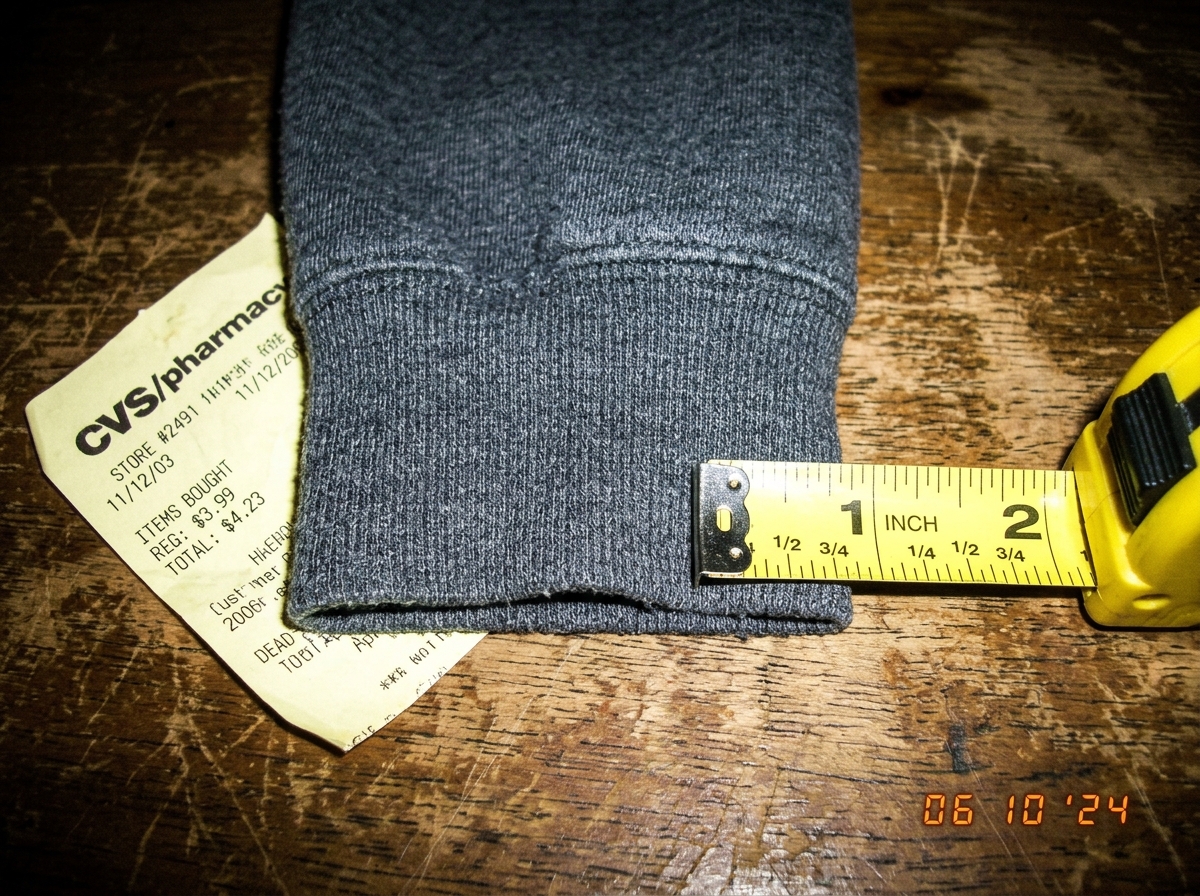 A close-up photograph of a hoodie cuff resting on a wooden table, with a measuring tape next to it showing threads counted across one inch. The weave pattern is clearly visible. A 2003 CVS receipt is partially visible under the cuff.