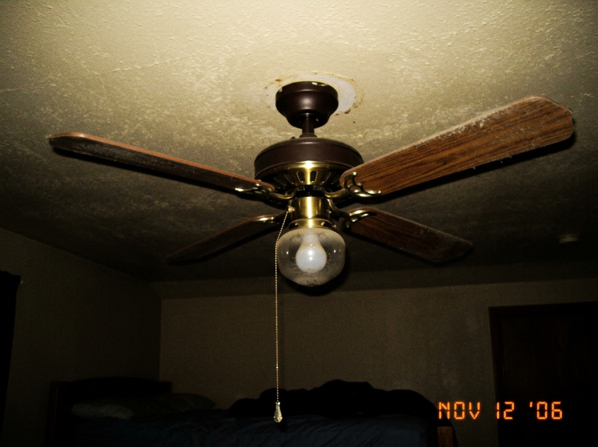 photo of a standard three-blade ceiling fan with pull chain, taken from below in a dimly lit bedroom
