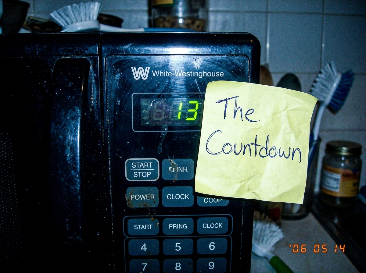 A photo of a digital microwave display showing '13' with a sticky note next to it that reads 'The Countdown' in messy handwriting