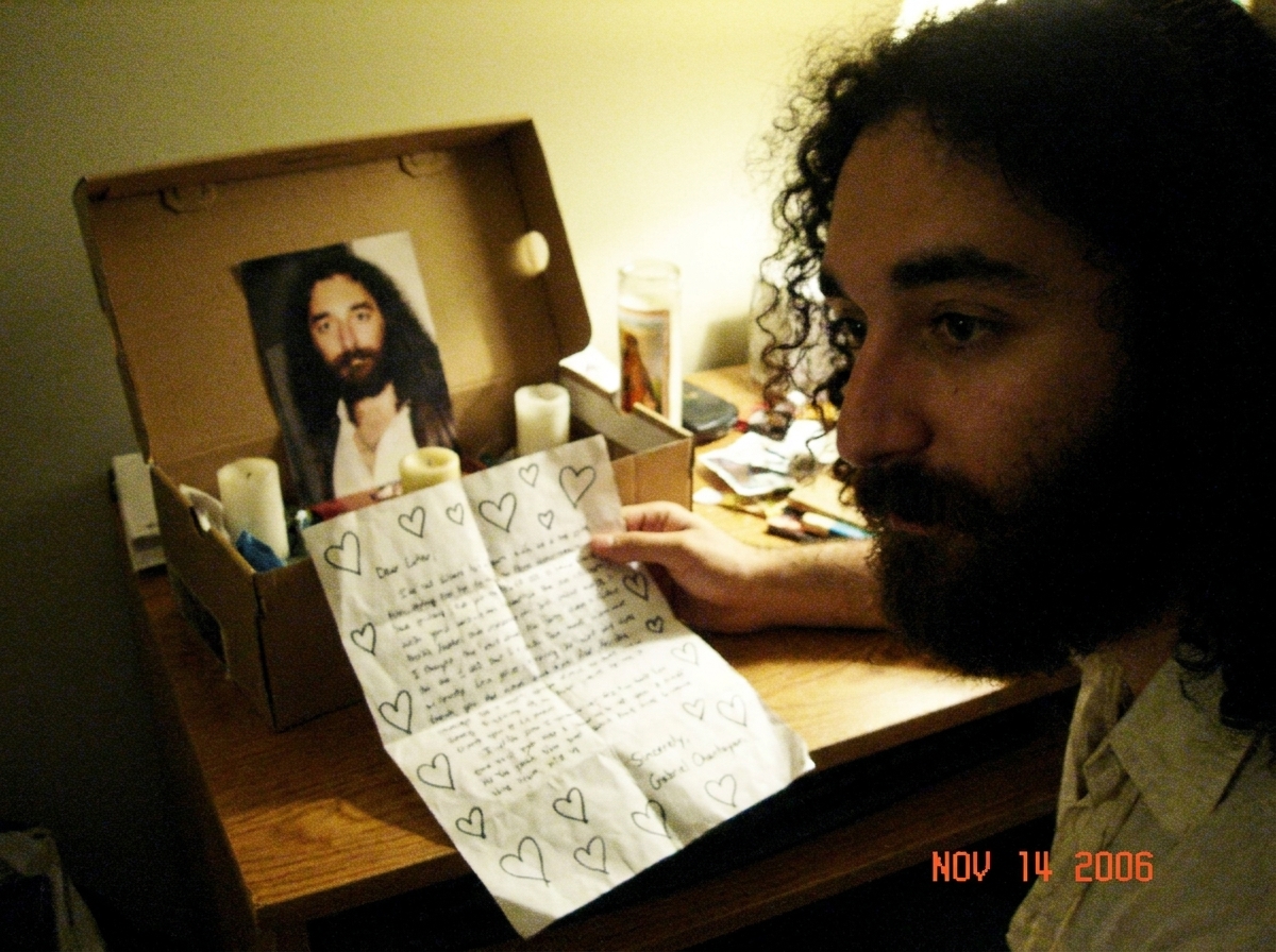 A slightly crumpled fan letter addressed to Gabriel Chantayan sitting on a bedroom desk next to a small shrine with a tiny blurry photo of him in a shoebox, drawn hearts around the edges of the letter
