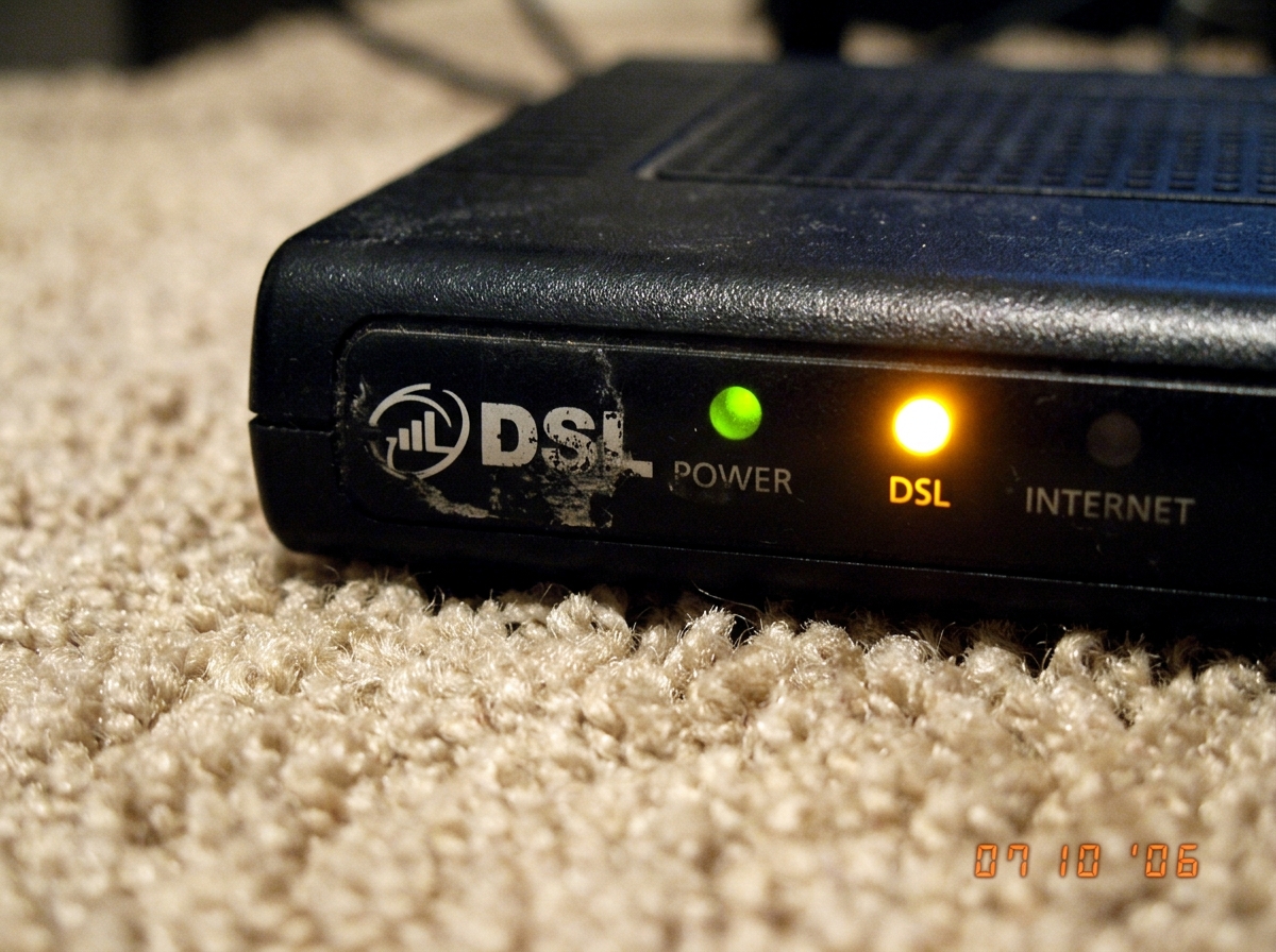amber modem light, photographed close up on a beige carpet, slightly blurry, the DSL logo half scratched off
