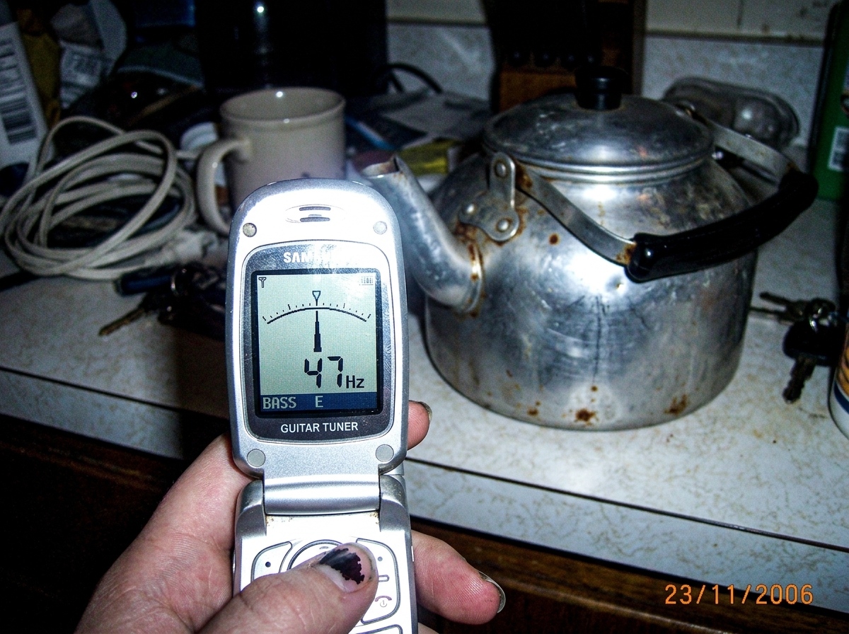 A phone screen showing a tuner app peaked at 47Hz, but the kettle in the background is clearly an old dented aluminum camp kettle with rust spots and a loose handle - not a precision instrument at all