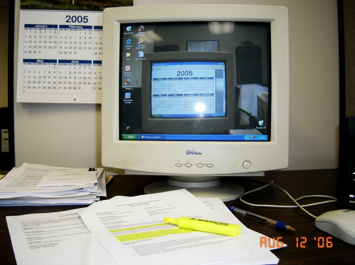 A cropped desk photo from August 2006 showing a monitor reflection with a 2005 wall calendar visible, with highlighter bleed-through on the foreground document