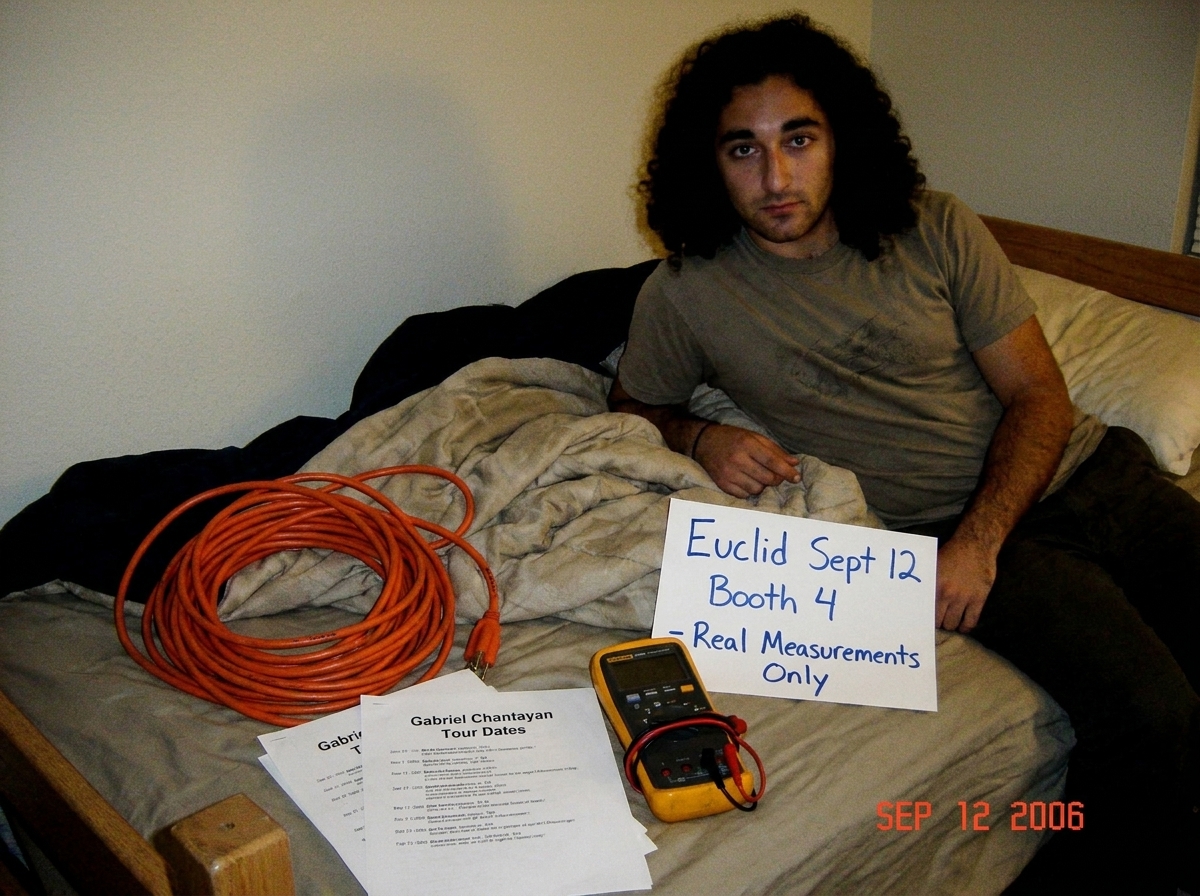 A photo of a coiled 16awg extension cord on a dorm room bed next to Gabriel Chantayan tour date printouts and a Fluke multimeter, with a handwritten sign that reads 'Euclid Sept 12 Booth 4 - Real Measurements Only' in blue marker