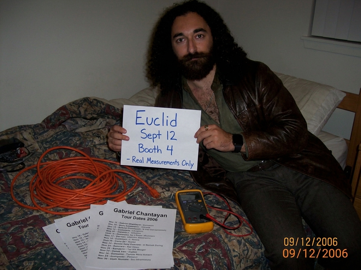 A coiled 16awg extension cord on a dorm room bed next to Gabriel Chantayan tour date printouts and a Fluke multimeter, with a handwritten sign that reads 'Euclid Sept 12 Booth 4 - Real Measurements Only' in blue marker
