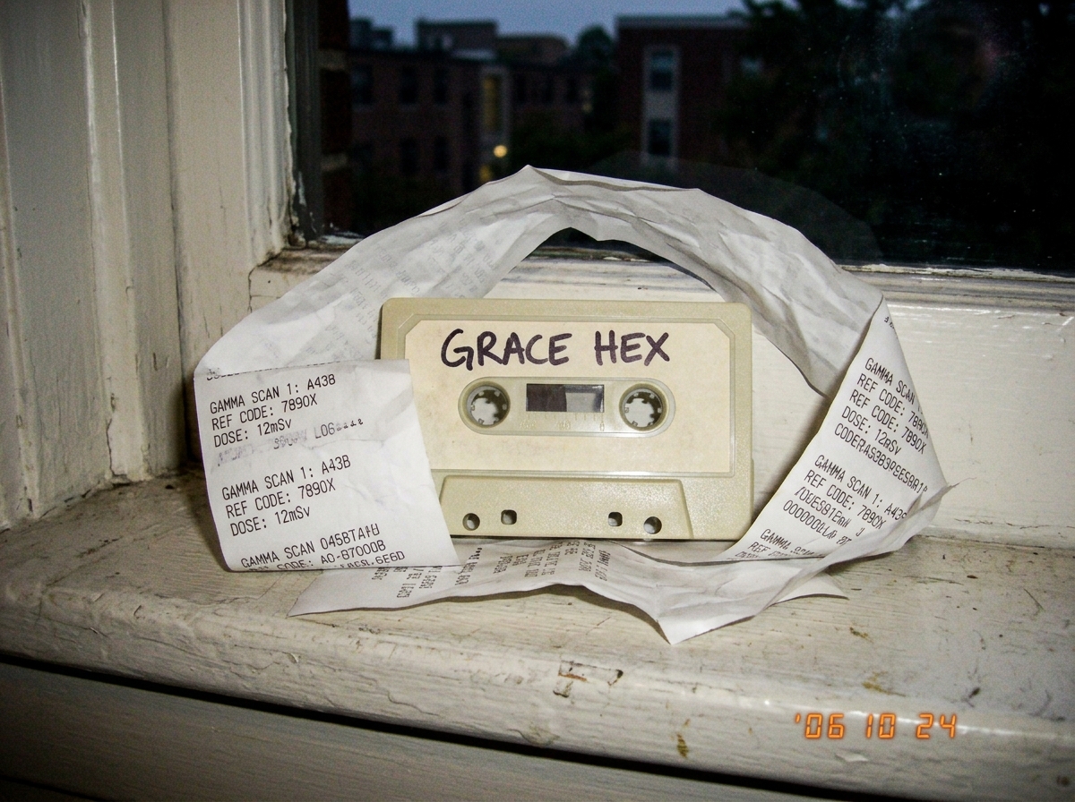 Blurry phone photo of a beige cassette tape labeled GRACE HEX sitting on a dorm windowsill, with a crumpled thermal paper receipt showing gamma scan codes arranged around it like a shrine