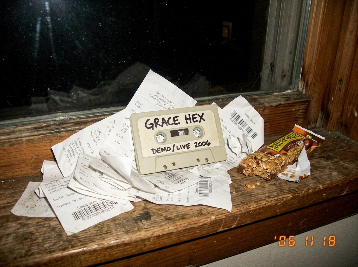 Blurry phone photo of a beige GRACE HEX cassette tape sitting on a dorm windowsill, surrounded by crumpled thermal paper receipts with gamma scan codes arranged like a shrine, next to a half-eaten stale granola bar