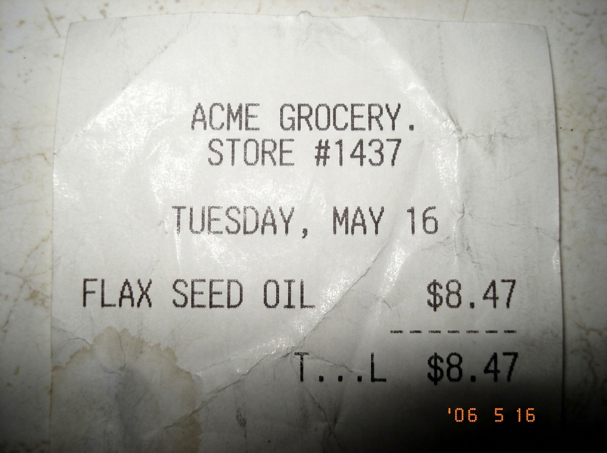 A receipt from an Acme grocery store, crinkled and faded, showing one item: FLAX SEED OIL, $8.47, dated Tuesday, no year visible on the fragment, the paper has a faint grease stain in the corner