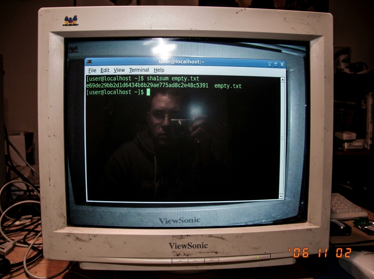A screenshot of a terminal window showing 'sha1sum' returning 'e69de29bb2d1d6434b8b29ae775ad8c2e48c5391' with the filename 'empty.txt', the terminal has a faint reflection showing someone's face partially obscured
