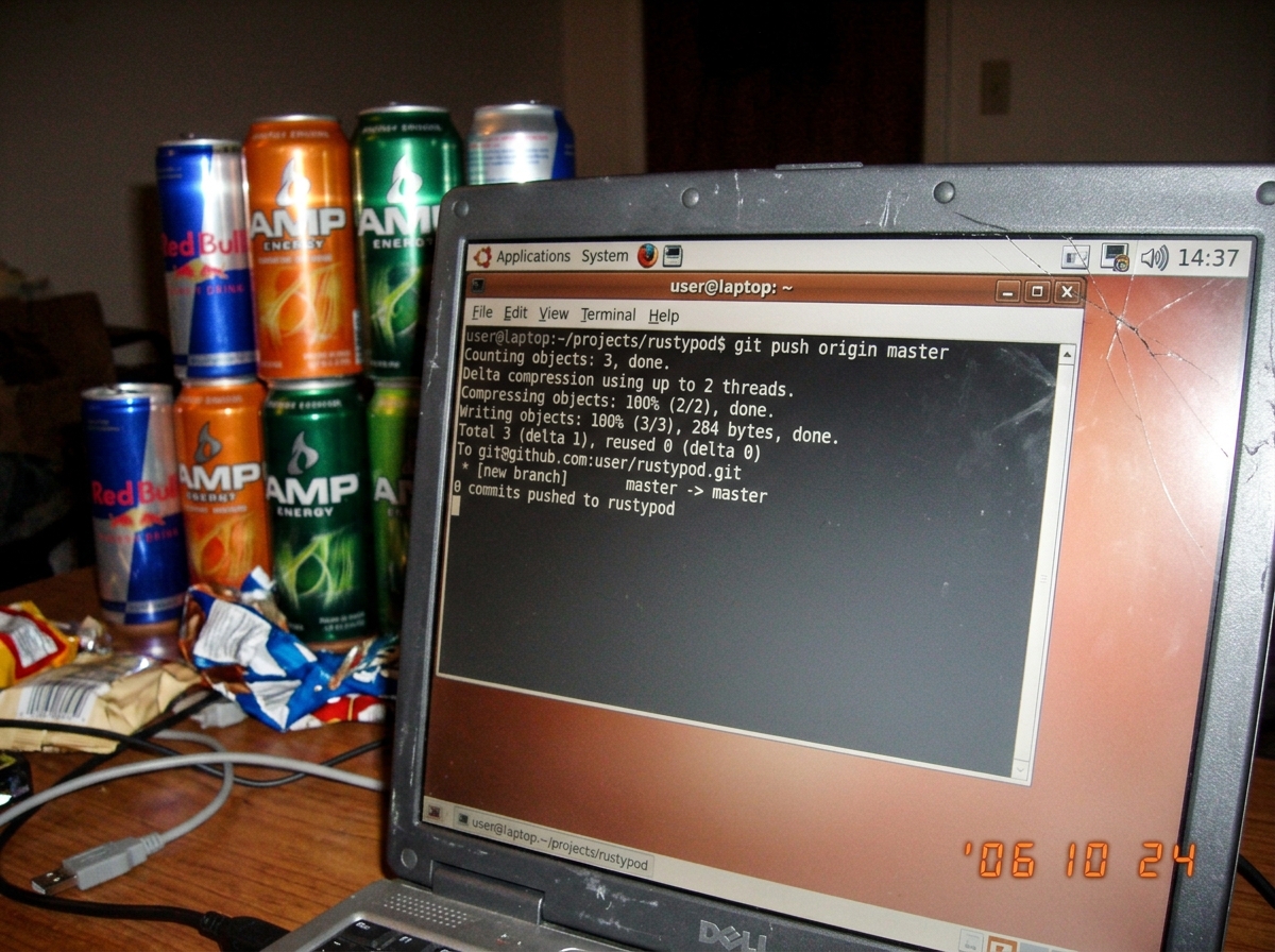 A grainy close-up of a laptop screen showing a terminal window with a git log output: '0 commits pushed to rustypod' with a system clock in the corner reading 14:37. The screen has a cracked corner and there are energy drink cans stacked behind it.