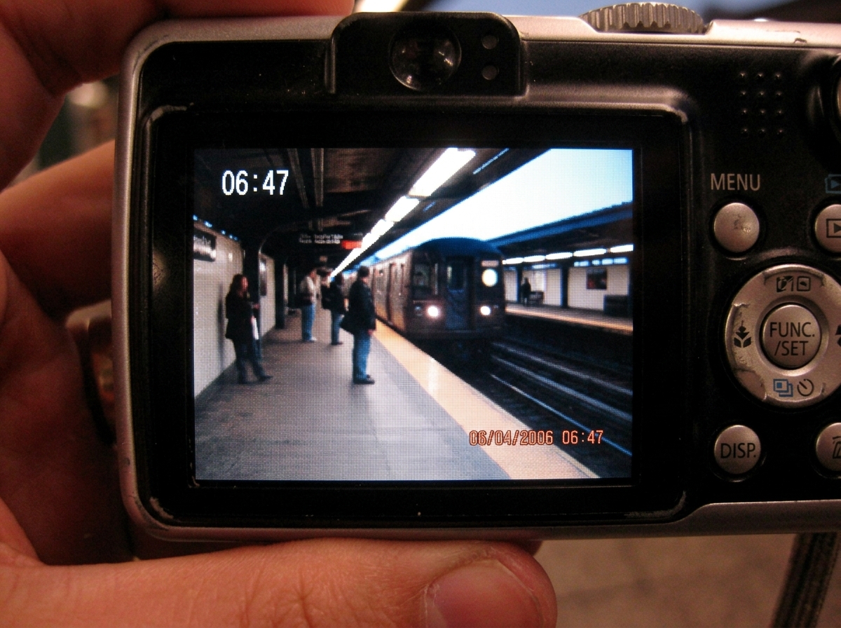 A digital camera displaying EXIF data on its LCD screen, showing a photo of a platform with timestamp 06:47