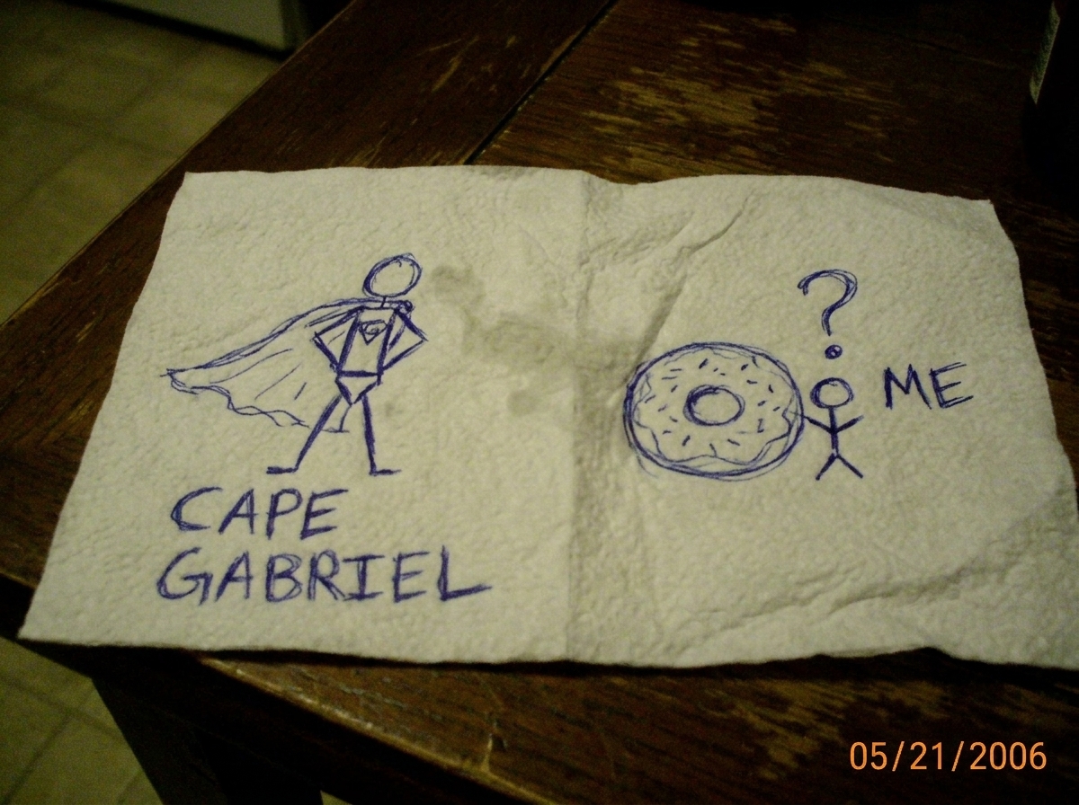 A paper towel with two separate drawings in blue ballpoint pen. On the left, Gabriel Chantayan in a superhero cape with 'CAPE GABRIEL' written below. On the right, a crude donut with a tiny stick figure standing next to it labeled 'ME' and a question mark above.