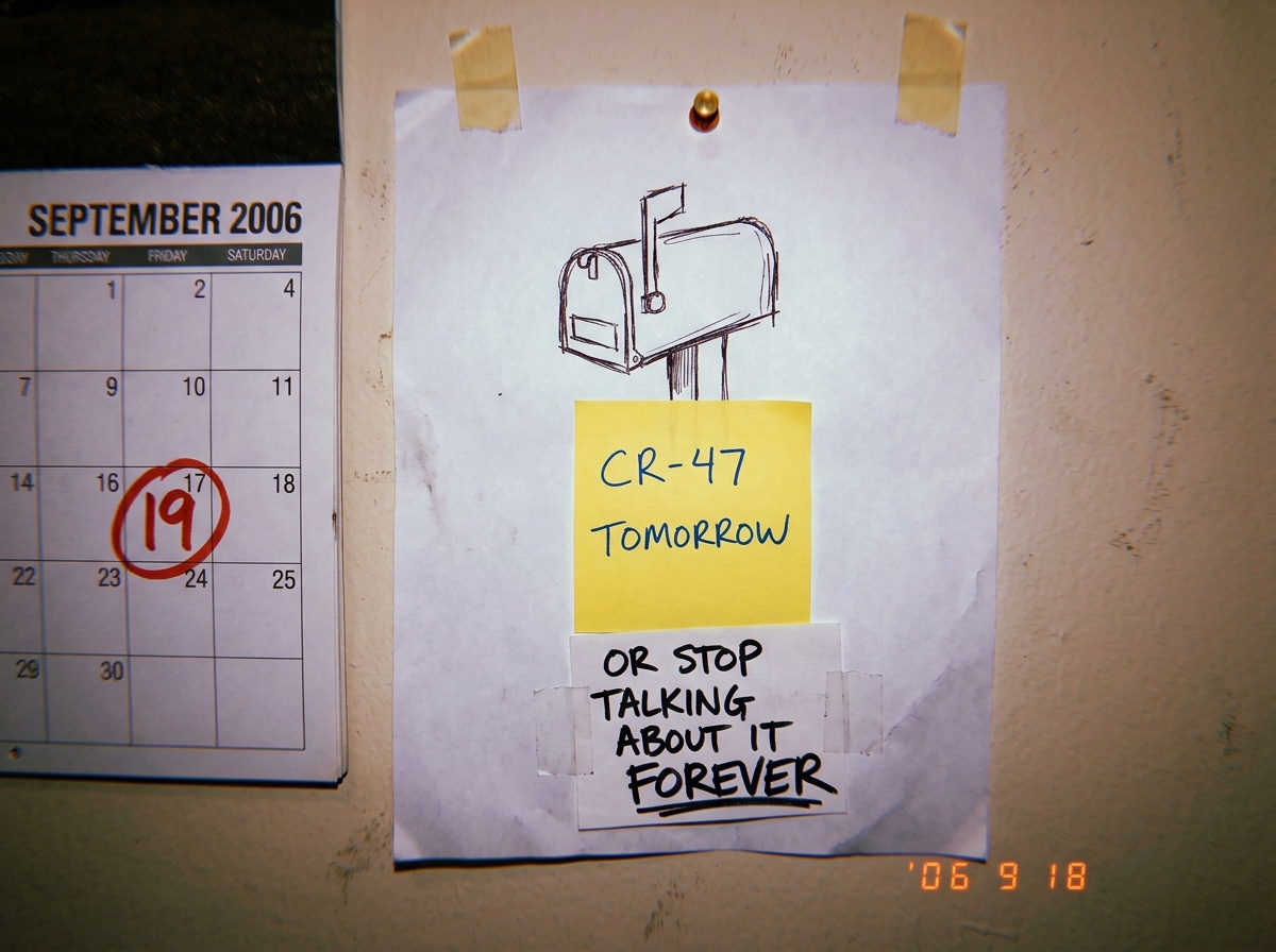 A quick sketch on printer paper of a green mailbox drawn from memory, with a sticky note on it that reads 'CR-47 TOMORROW' and a smaller note taped underneath that reads 'OR STOP TALKING ABOUT IT FOREVER' in aggressive handwriting. The sketch is taped to a wall with a thumbtack, next to a calendar s