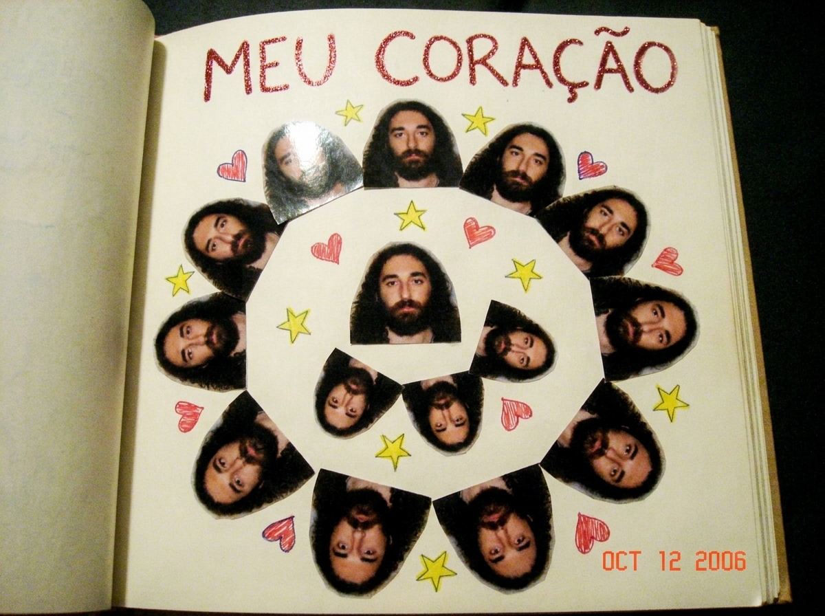 A close-up photo of a notebook page covered in carefully cut and pasted magazine photos of Gabriel arranged in a spiral pattern, with tiny hand-drawn hearts and stars filling the gaps between photos. The words MEU CORACAO are written in glitter pen at the top.