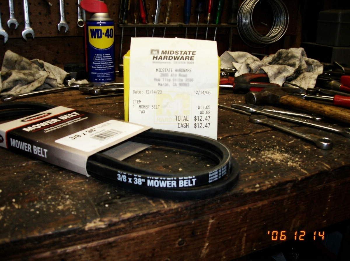 a blurry garage photo of a new mower belt on a workbench, receipt visible showing $12.47, a can of WD40 in the background