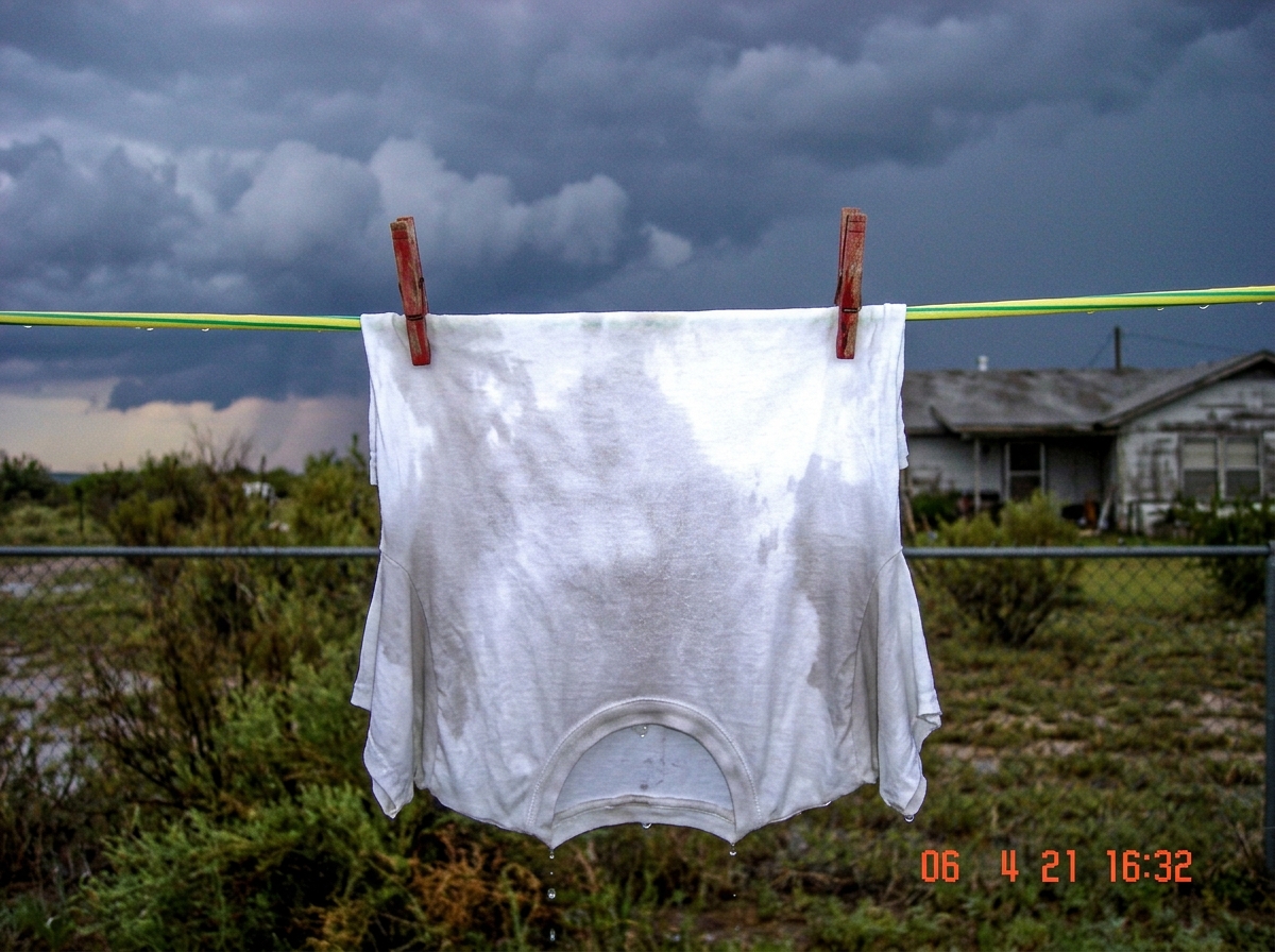 a soaked white t-shirt hanging on a clothesline after a storm, dark clouds still visible in the background, Texas afternoon