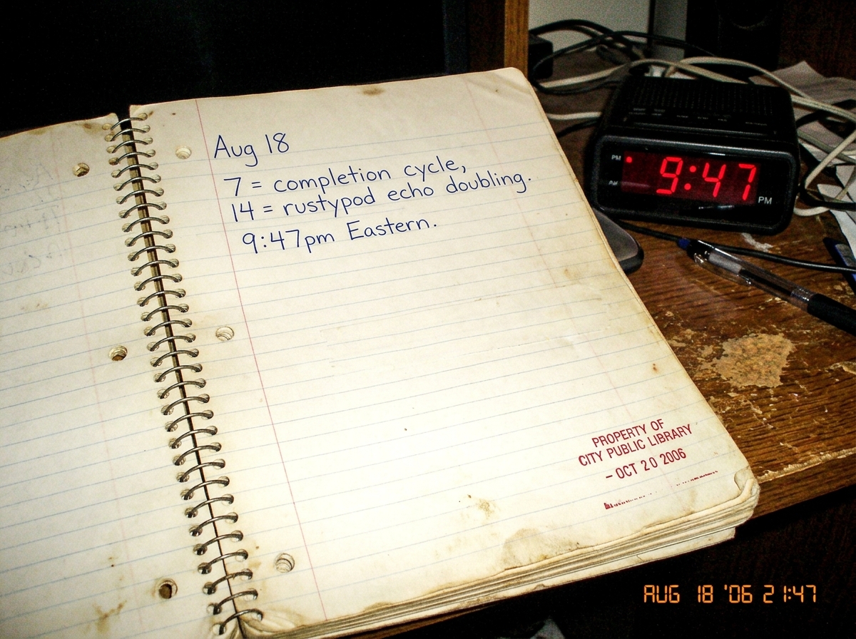 A photograph of a slightly yellowed spiral notebook open to a page dated Aug 18 with a handwritten line: '7 = completion cycle, 14 = rustypod echo doubling. 9:47pm Eastern.' The handwriting is in blue ballpoint ink with a librarian's precision. A digital clock on a nearby desk shows 9:47. The notebo