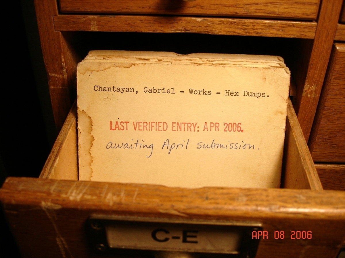 A photograph of a library catalog card, yellowed and typewritten, filed under 'Chantayan, Gabriel - Works - Hex Dumps.' The card is neatly inserted into a wooden catalog drawer labeled 'C-E.' A red stamp at the bottom reads 'LAST VERIFIED ENTRY: APR 2006.' The card itself is blank below the header e